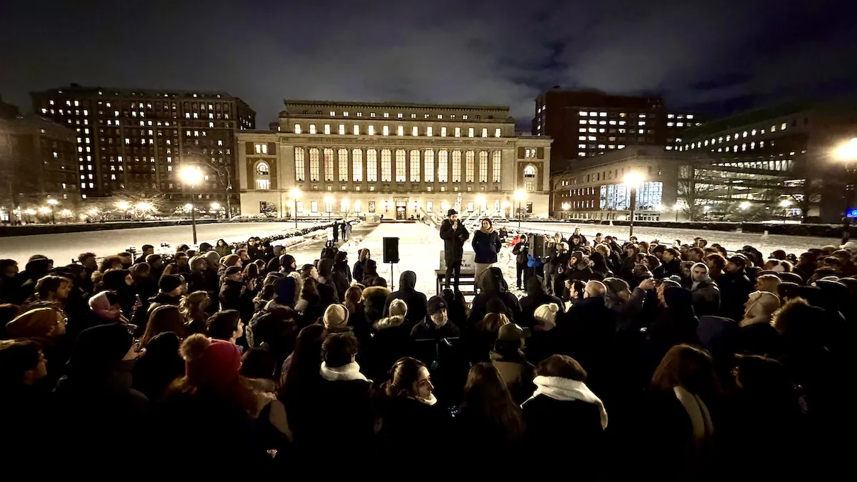 large crowd outside in the evening, listening to a speaker